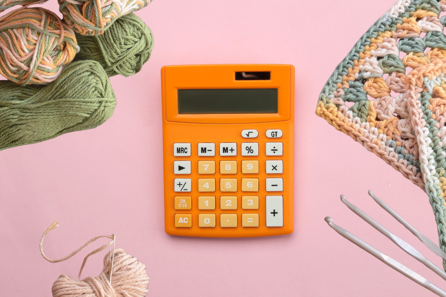 Orange calculator surrounded by yarn and crochet hooks
